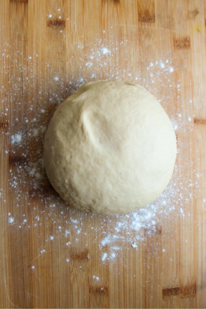 Risen ball of dough on a lightly floured wooden board.