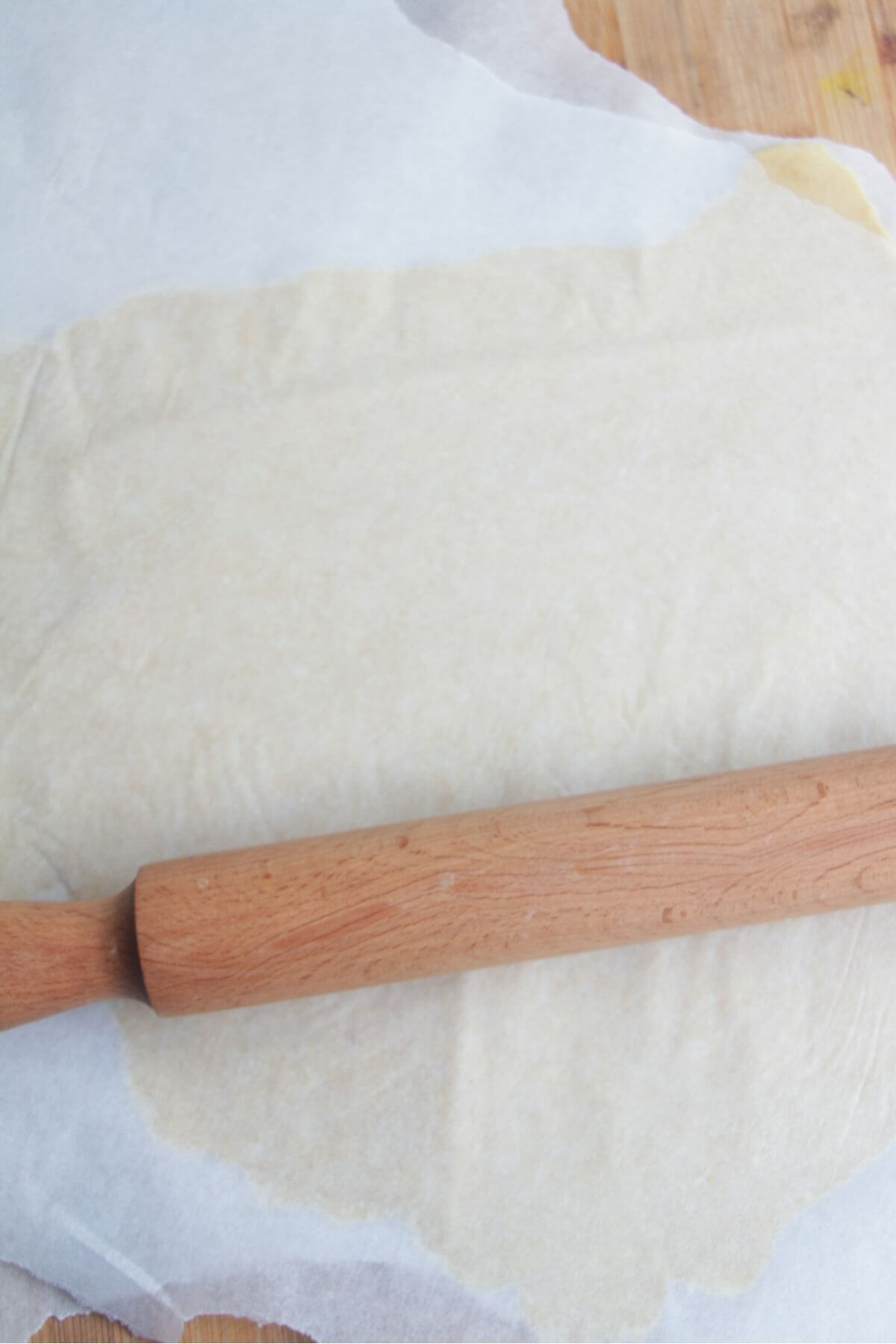 A rolling pin on a sheet of baking paper with rolled out pastry underneath.