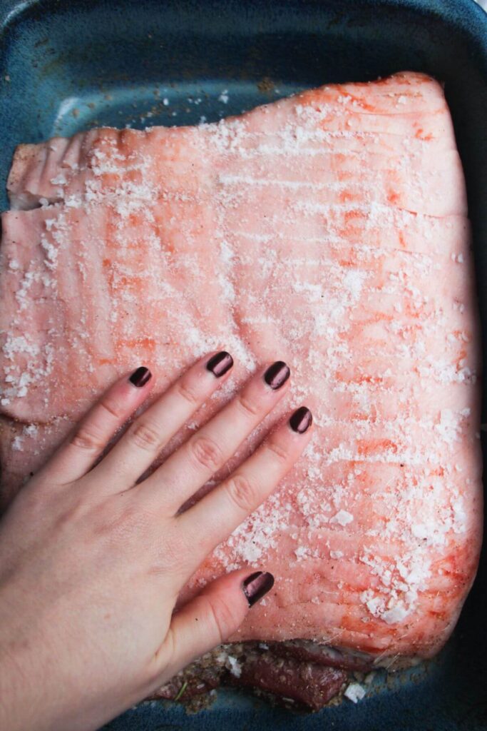 A hand rubbing salt all over scored pork belly skin.