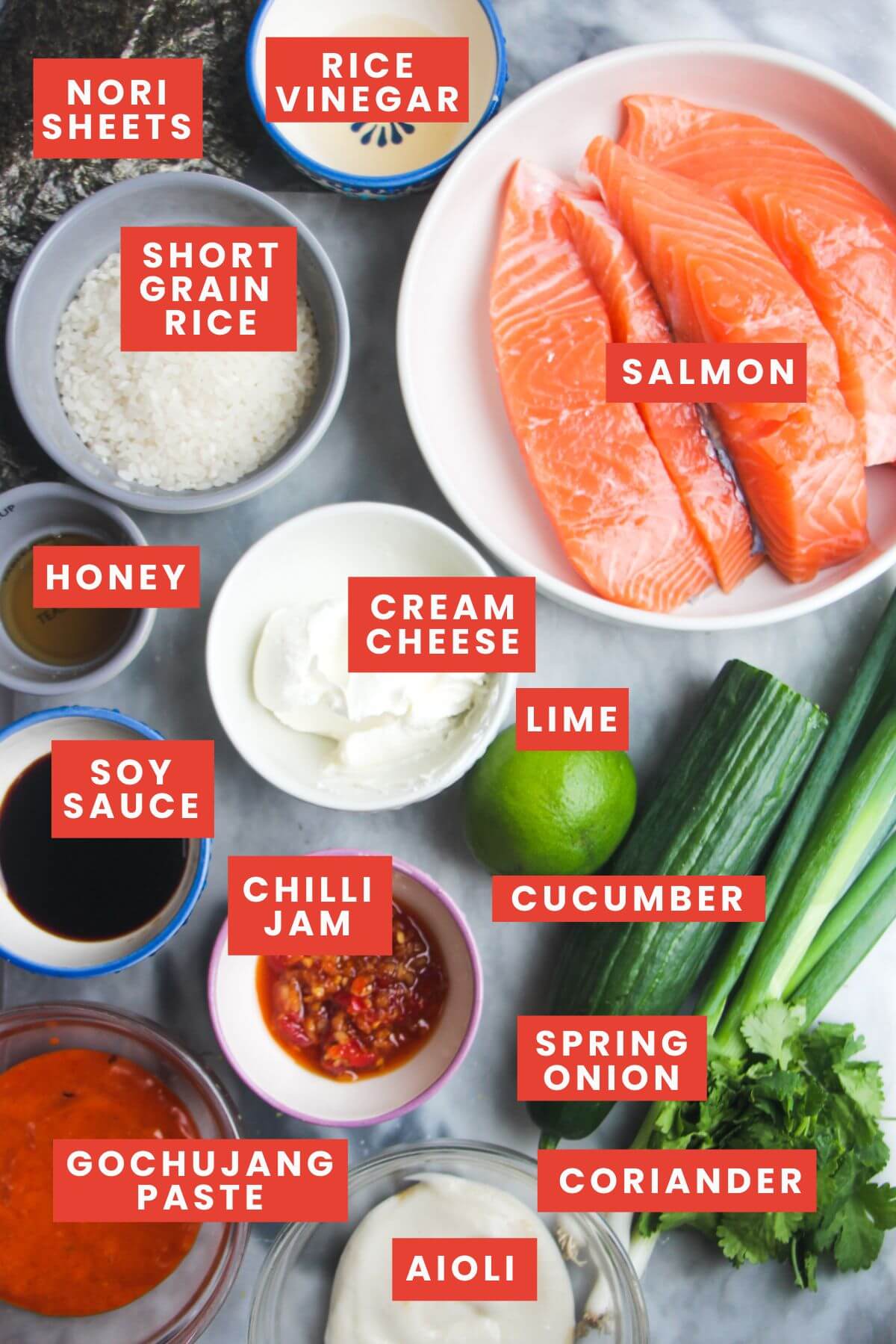 Ingredients for salmon sushi bake laid out on a grey marble background and labelled.