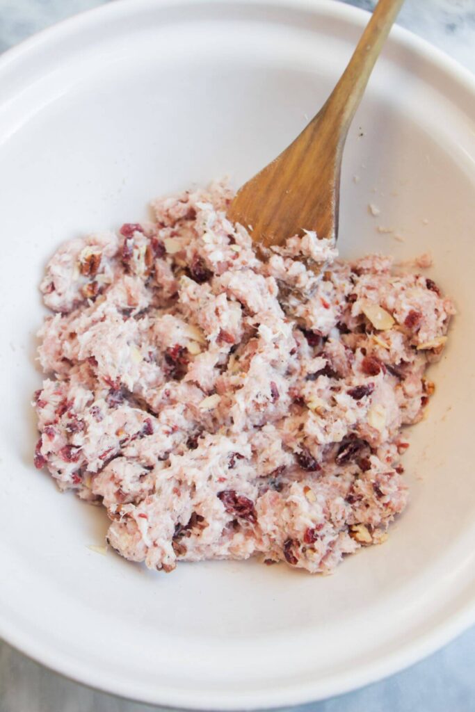 Sausage meat, cranberries and pecans mixed in a large white bowl.