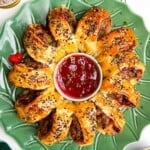 Sausage roll wreath on a plate with cranberry sauce in the middle.