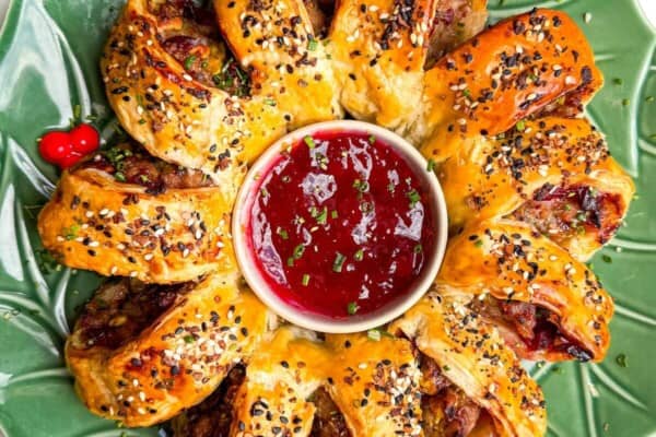 Sausage roll wreath on a plate with cranberry sauce in the middle.