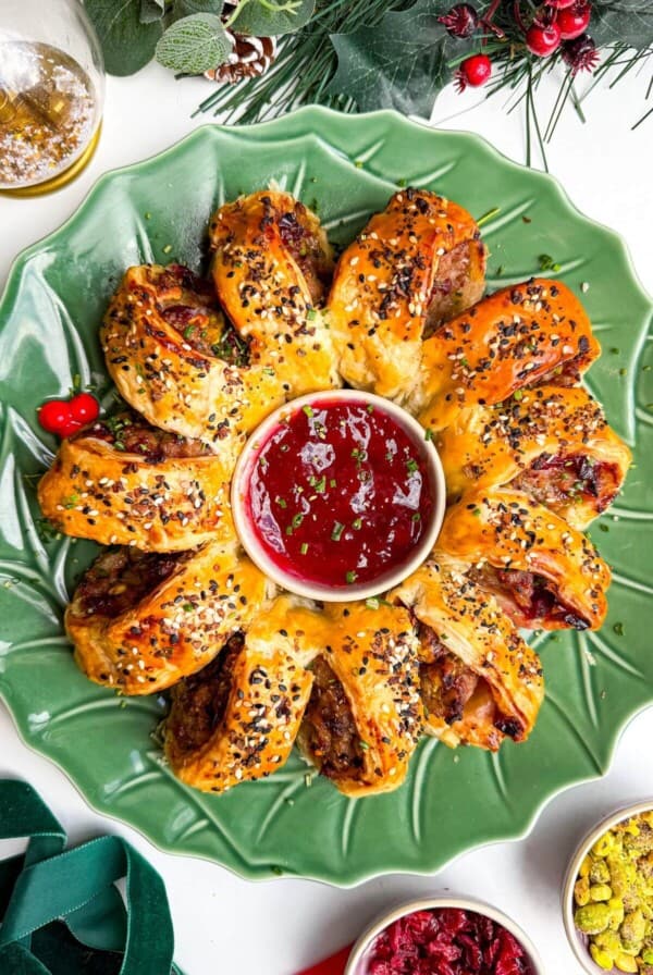 Sausage roll wreath on a plate with cranberry sauce in the middle.