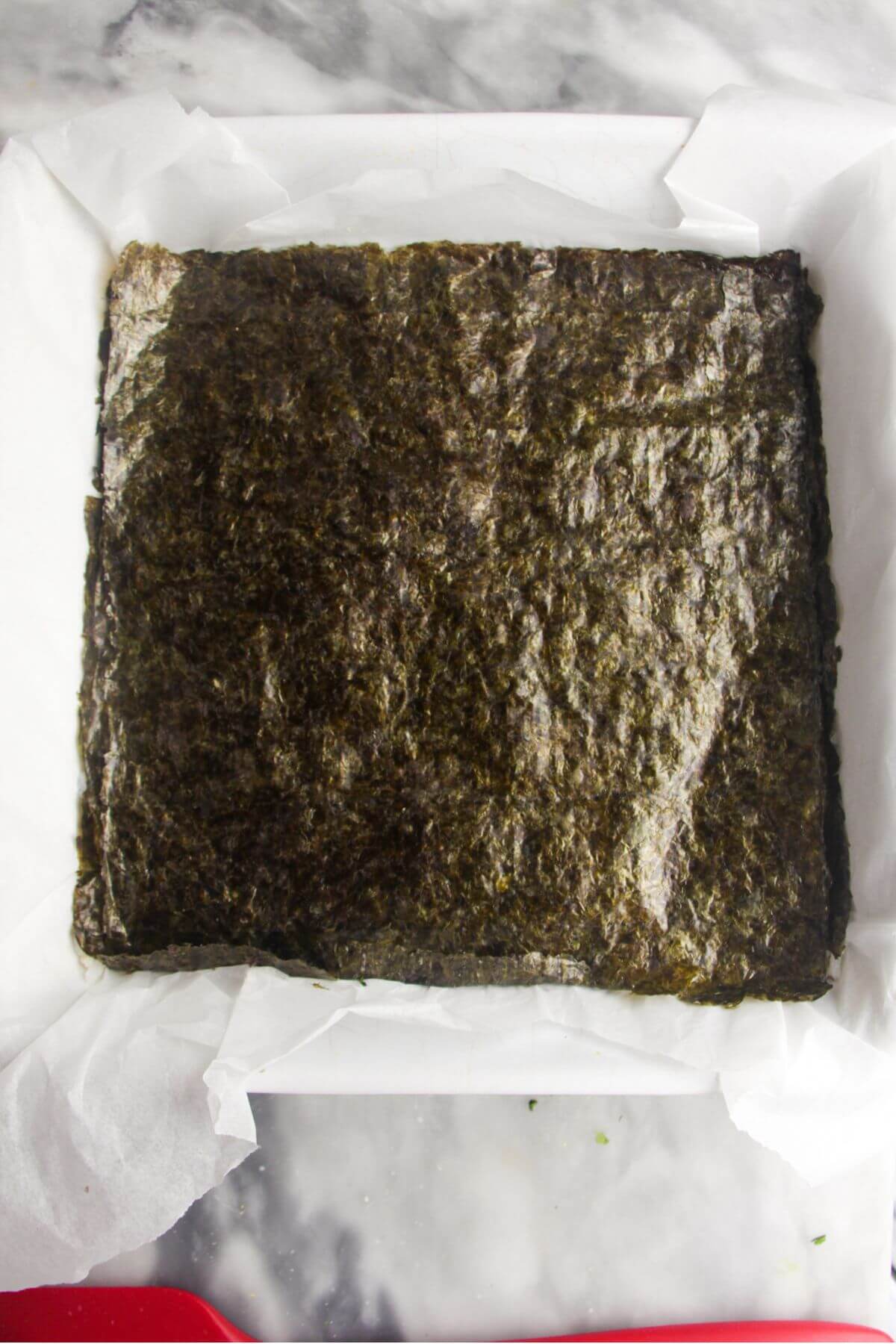 Seaweed sheets on top of the rice layer in a baking paper lined square oven dish.