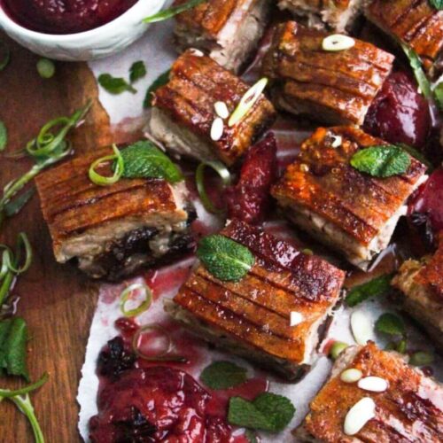 Square pieces of slow roasted pork belly on a wooden serving platter.