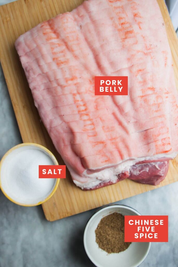 Ingredients for crispy slow roasted pork belly laid out on a grey marble background and labelled.
