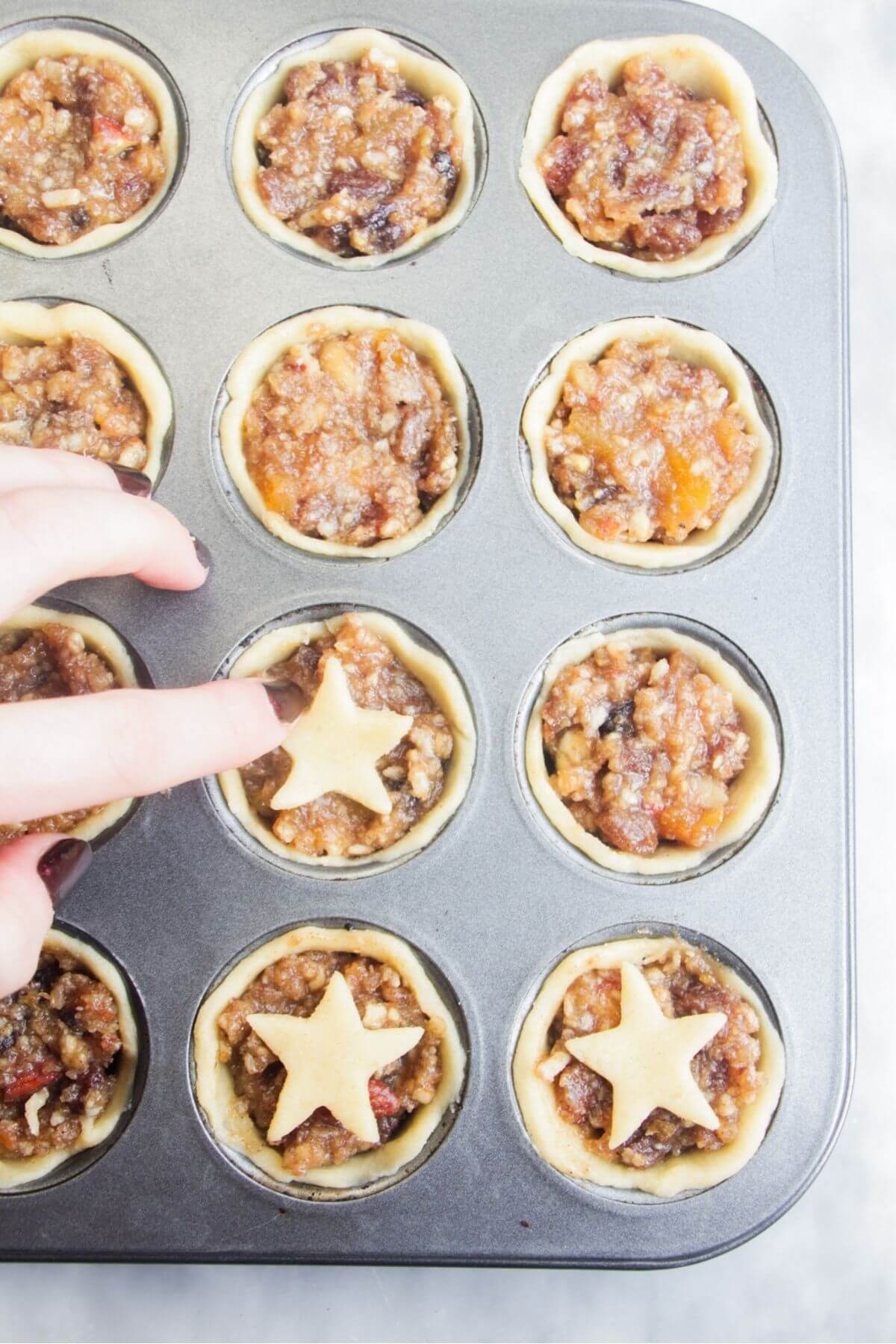 Hand placing small pastry star on top of fruit mince pie.