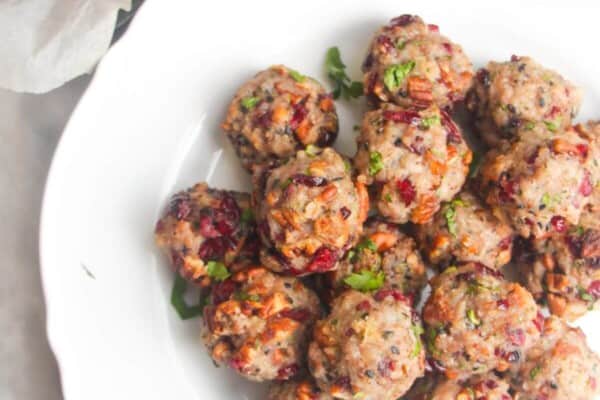 Cranberry pecan stuffing balls piled on a large white plate with more stuffing balls in the background.