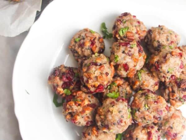 Cranberry pecan stuffing balls piled on a large white plate with more stuffing balls in the background.