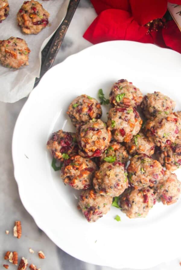 Cranberry pecan stuffing balls piled on a large white plate with more stuffing balls in the background.