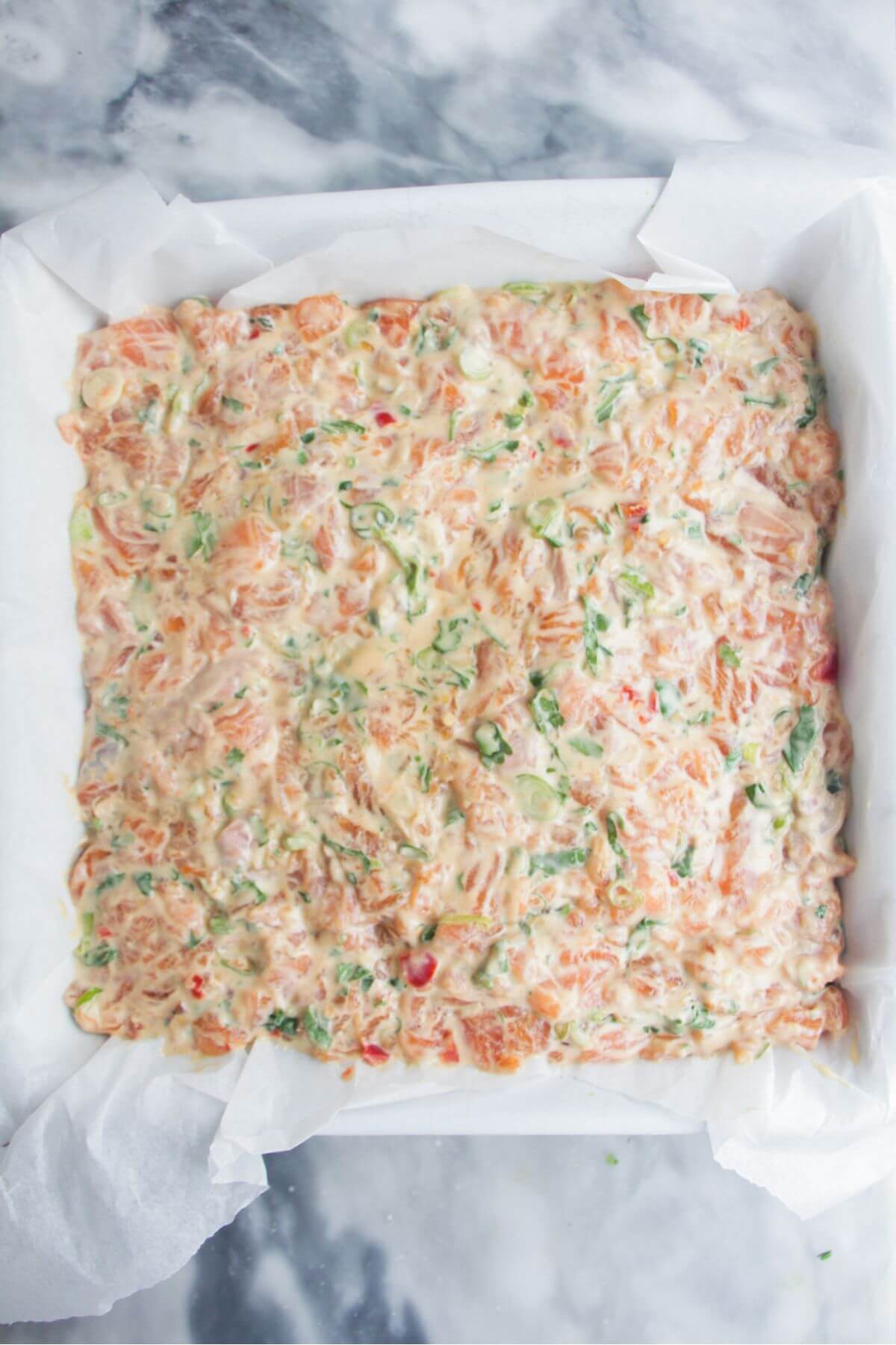Salmon mix smoothed on top of rice in a baking paper lined square oven dish.