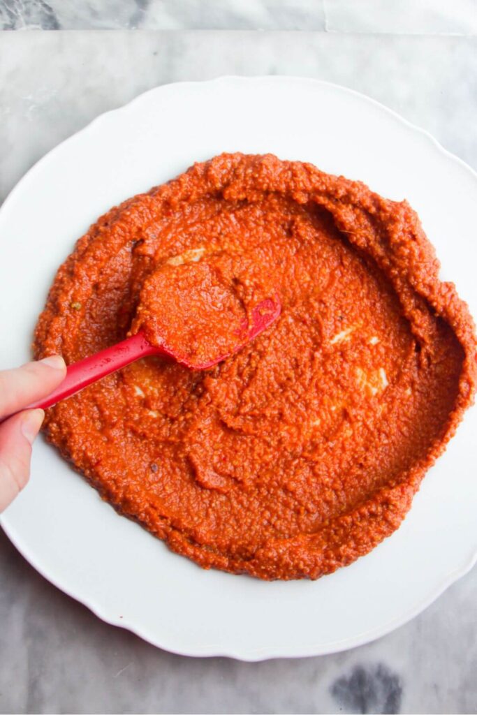 Smoothing tomato pesto onto a white serving plate with a red spatula.