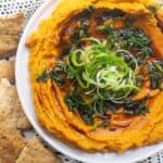 Spiced roasted carrot dip on a white and black patterned background with crackers on the side.