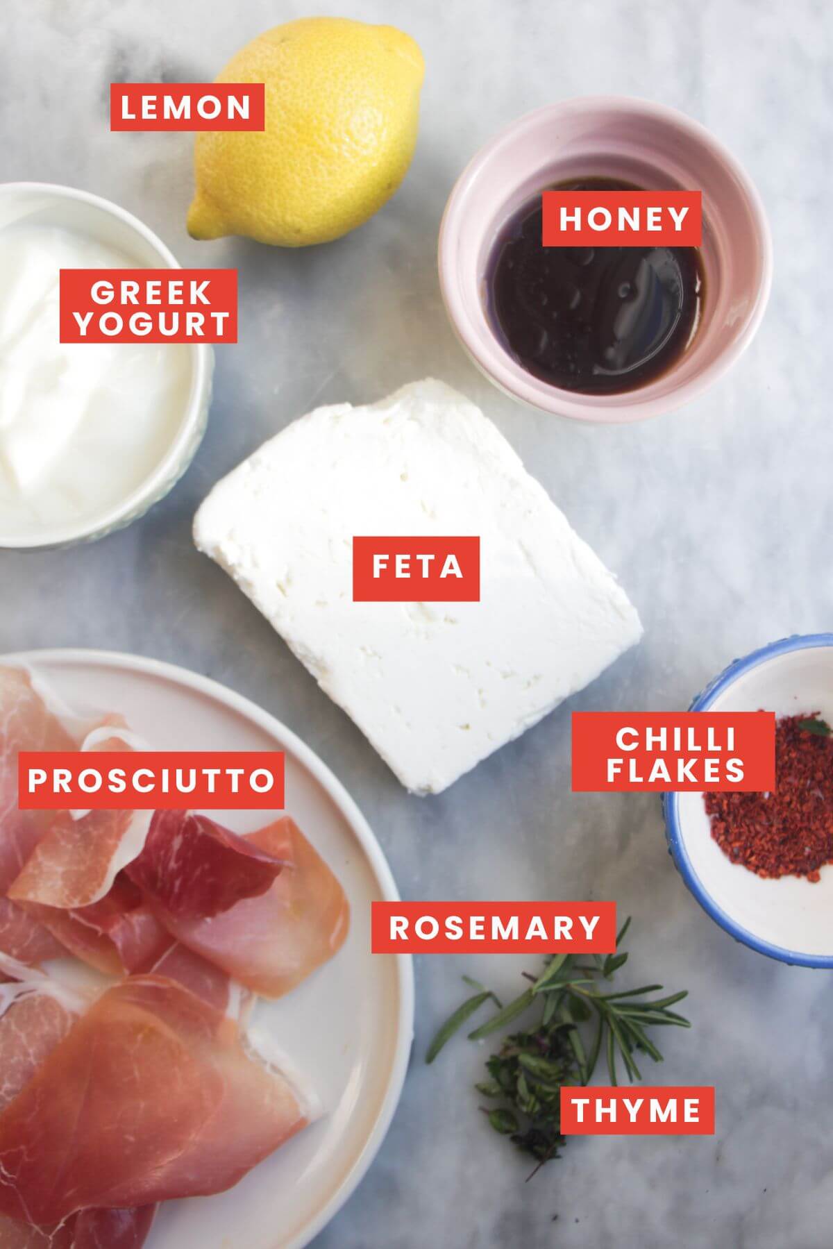 Ingredients for whipped feta dip laid out on a grey marble background and labelled.