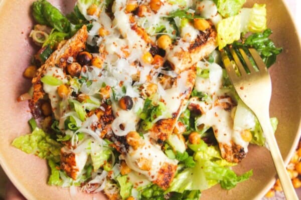 Hand holding a pink bowl filled with grilled chicken Caesar salad.