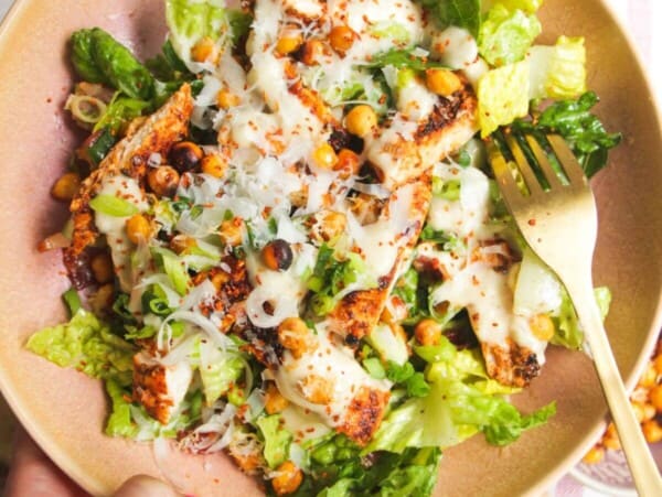 Hand holding a pink bowl filled with grilled chicken Caesar salad.