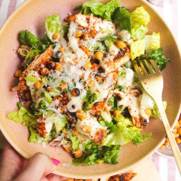 Hand holding a pink bowl filled with grilled chicken Caesar salad.
