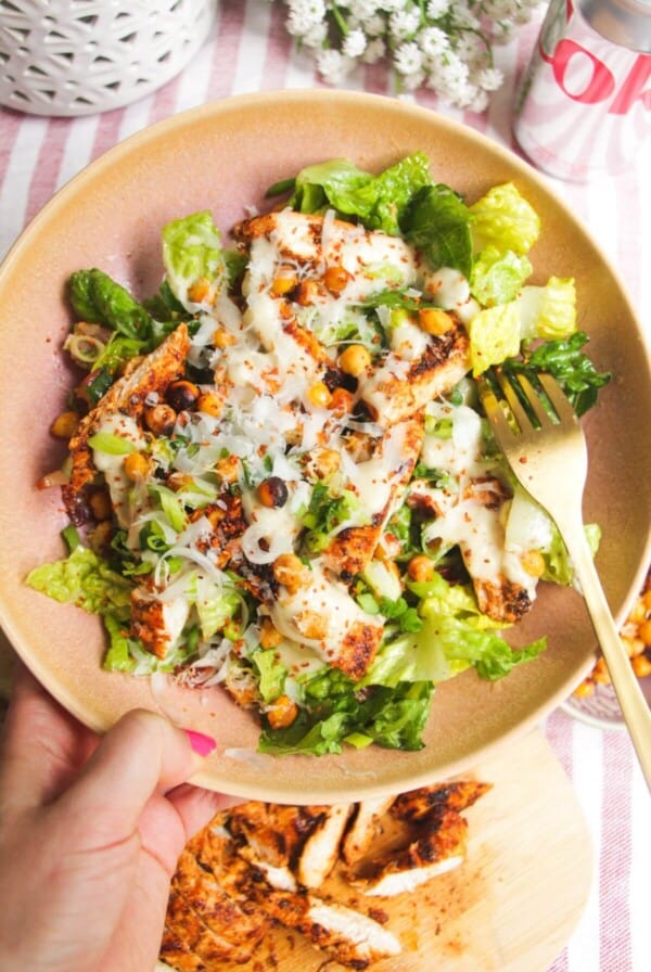 Hand holding a pink bowl filled with grilled chicken Caesar salad.