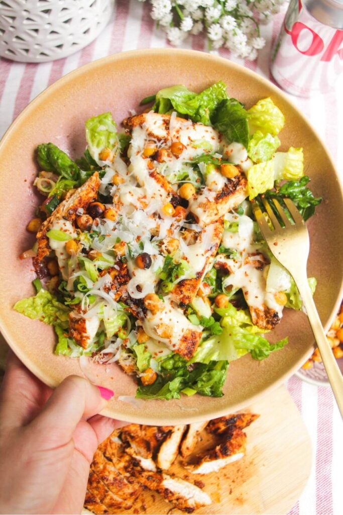 Hand holding a pink bowl filled with grilled chicken Caesar salad.