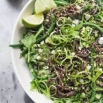 Cold Asian soba noodle salad with lots of green vegetables in a large serving platter, with jug of dressing on the side.