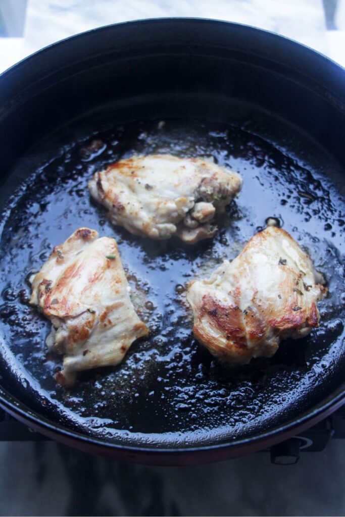Golden chicken thighs cooking in a large black skillet.