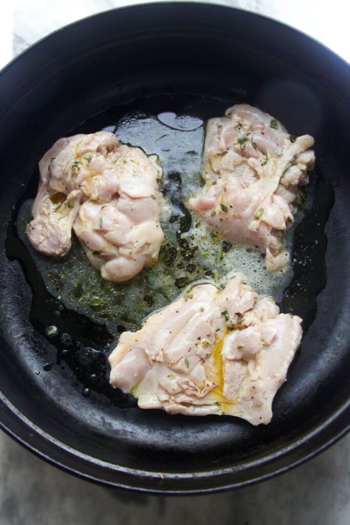 Chicken thighs cooking in a large black skillet.