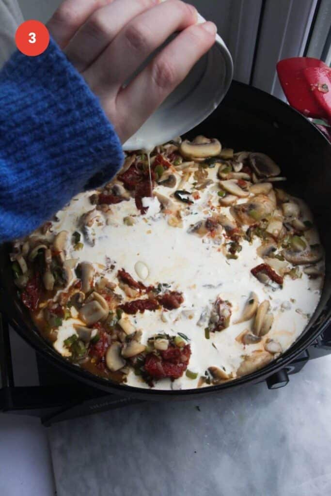 Pouring cream into mushrooms and sundried tomatoes in a pan.