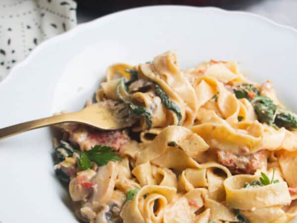 Close up of a bowl of creamy mushroom pasta, with a fork in it.