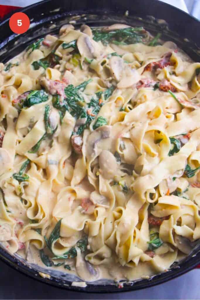 Fettuccine tossed through mushroom Alfredo sauce in a pan.