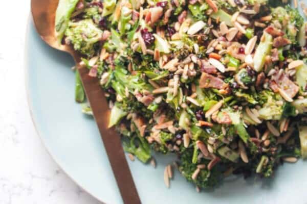 Grilled broccoli crunch salad in a large blue serving plate with focaccia and sunflower seeds on the side.