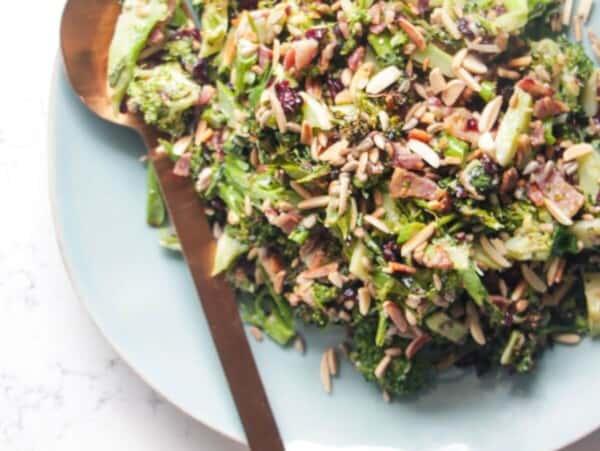 Grilled broccoli crunch salad in a large blue serving plate with focaccia and sunflower seeds on the side.