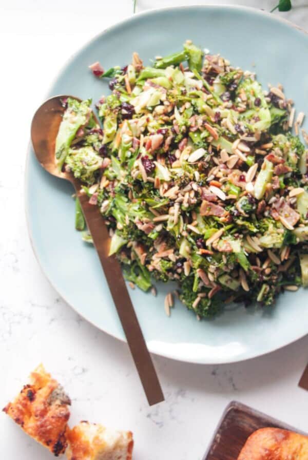Grilled broccoli crunch salad in a large blue serving plate with focaccia and sunflower seeds on the side.