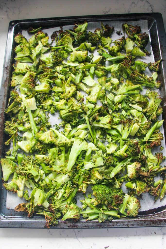 Grilled broccoli laid out on a lined oven tray.