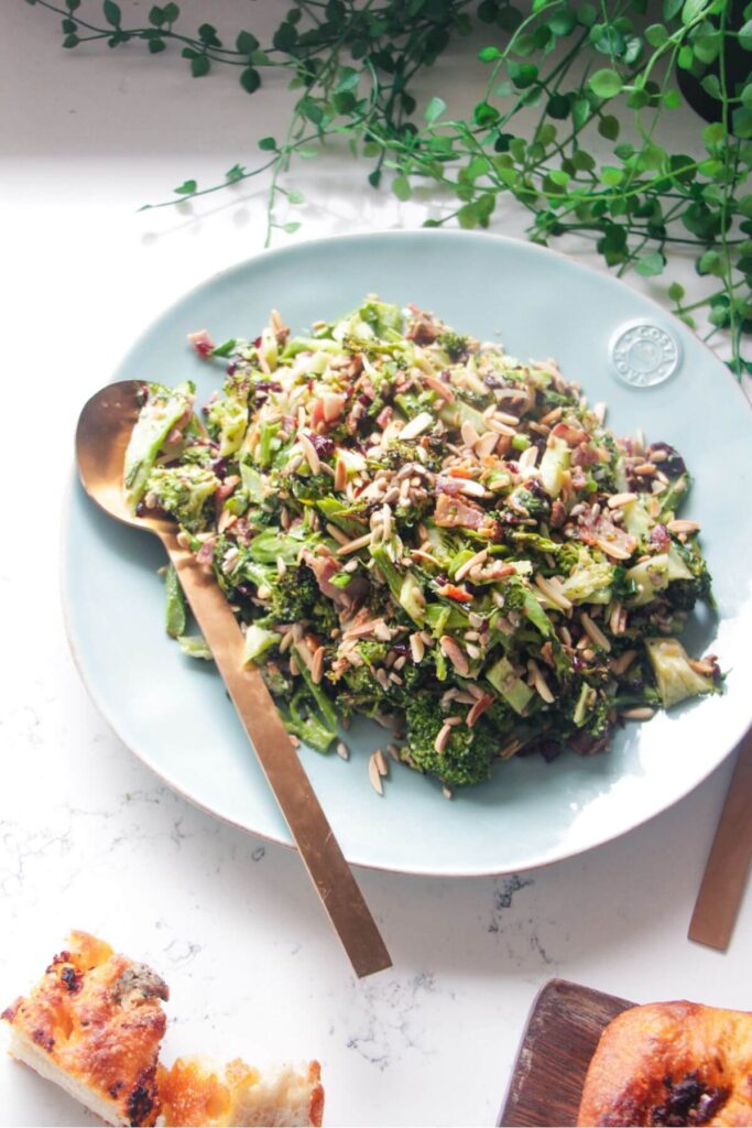 Grilled broccoli crunch salad in a large blue serving plate with focaccia and sunflower seeds on the side.