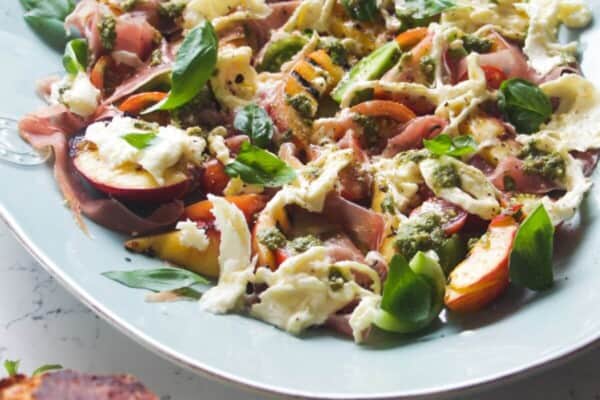 Grilled peach, burrata, tomato salad on a large blue serving platter.