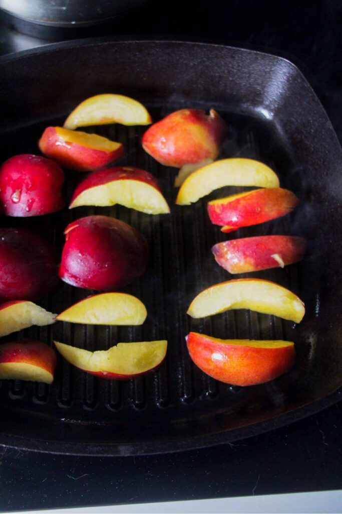 Peach slices grilling on a black griddle pan.