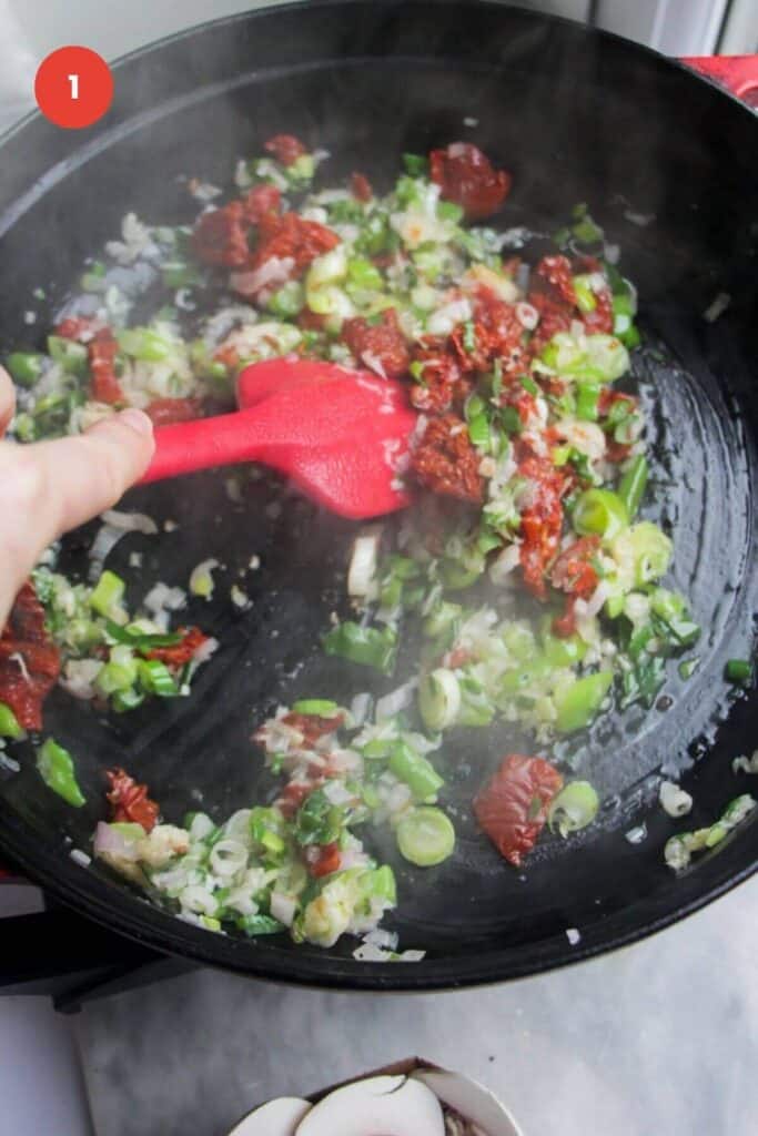 Sundried tomatoes and scallions cooking a large pan.