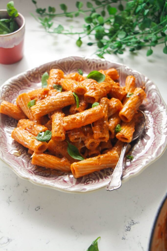 Close up view of spicy rigatoni on a pink plate.