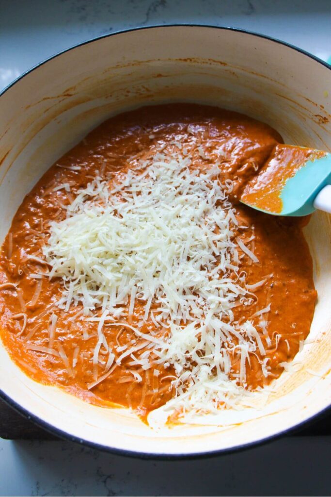 Grated parmesan added to tomato harissa cream sauce in a large white skillet.