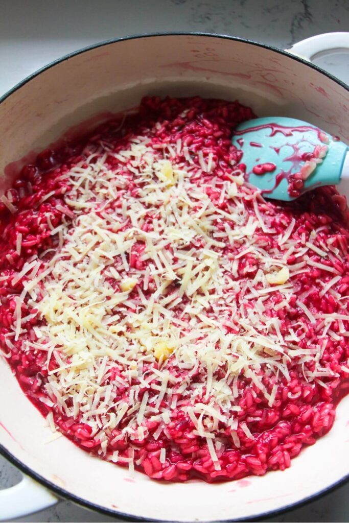 Grated parmesan on top of bright pink beetroot risotto in a large white skillet.