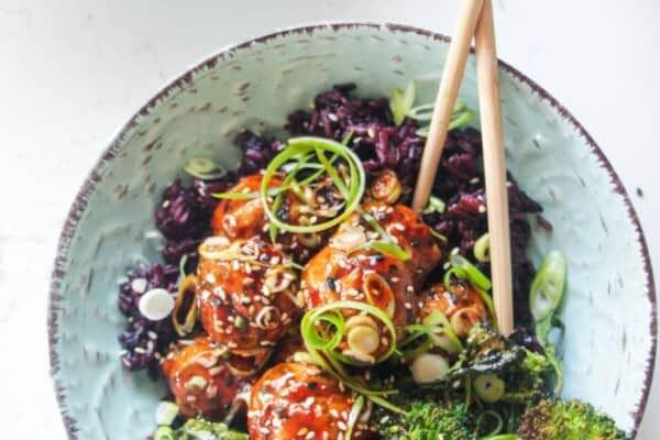 Glazed Asian chicken meatballs with rice and broccoli in a small blue bowl.