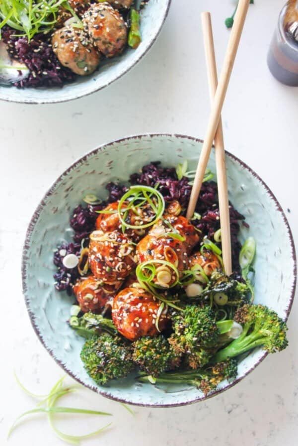 Glazed Asian chicken meatballs with rice and broccoli in a small blue bowl.