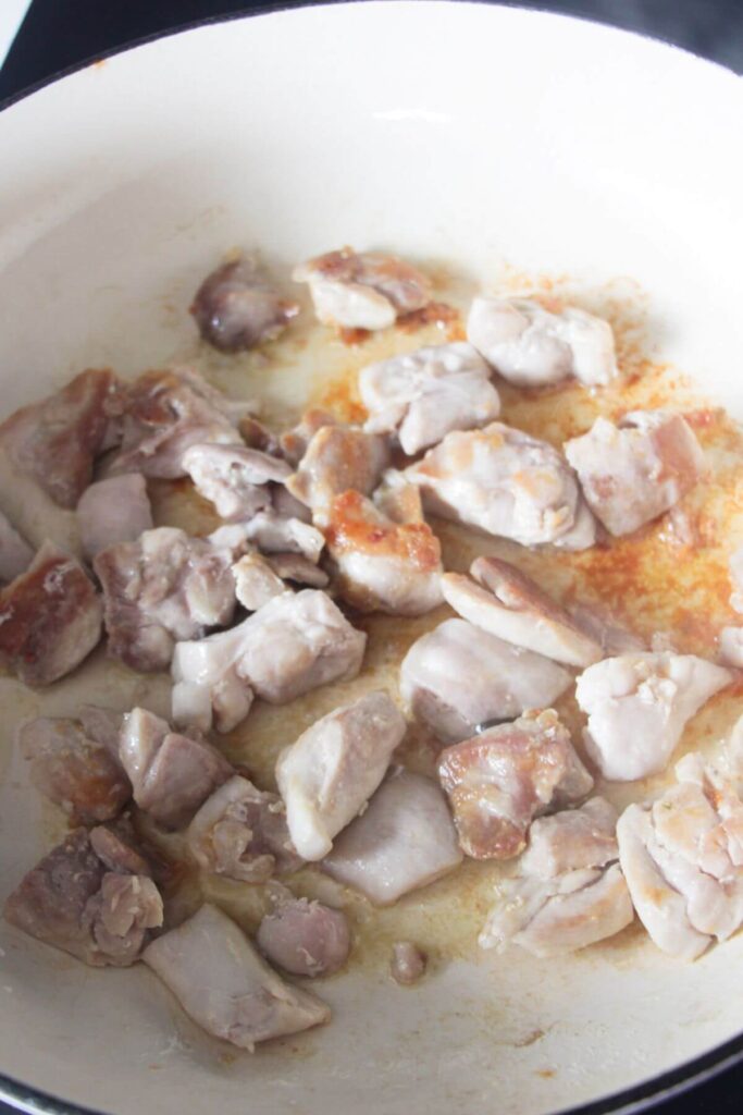 Browned diced chicken in a white skillet on the stove top.