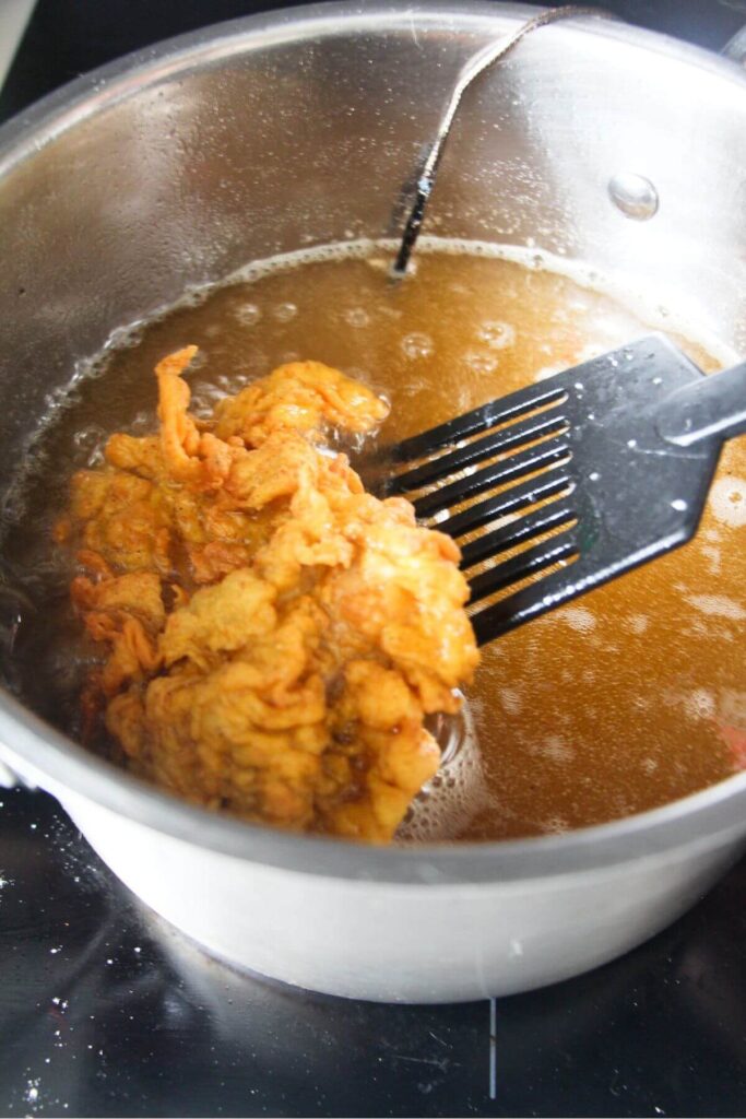 Piece of fried chicken being turned in hot oil by a black spatula.