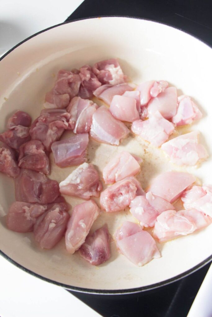 Diced chicken in a white skillet on the stove top.