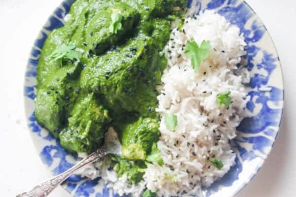 Chicken saag on a white and blue plate with rice, with more curry and naan on the side.