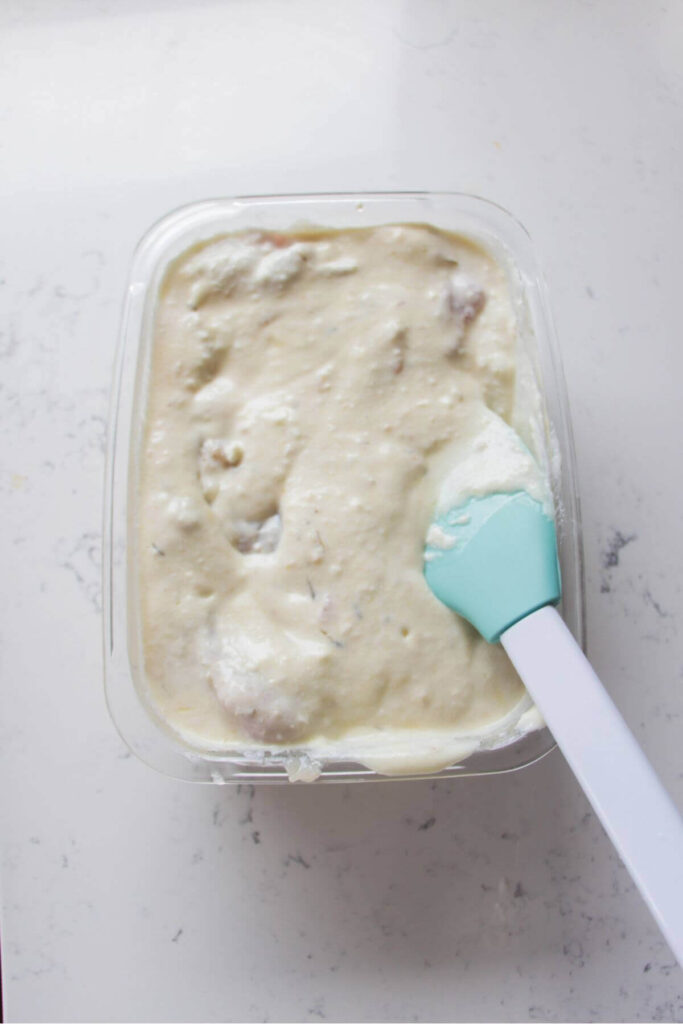 Chicken thighs in yogurt marinade in a glass container.