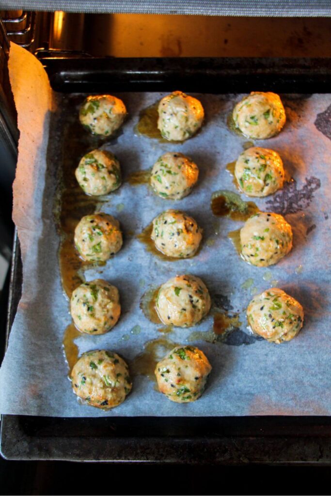 Par-cooked chicken meatballs on a lined oven tray in the oven.