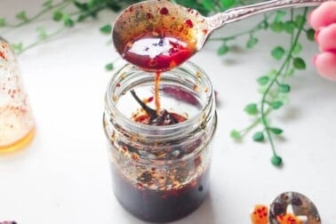 Hot honey drizzling from a silver spoon into a glass jar.